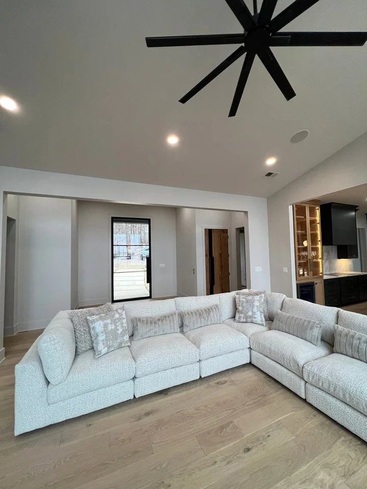 The Pickwick living room looking toward a glazed entry and timber door, with light seating and a lit kitchen display cabinet to the right.