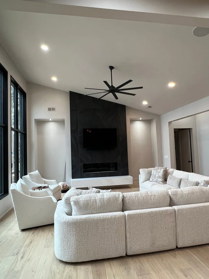 The Pickwick living room with a dark full-height fireplace wall, pale hearth, recessed niches, tall windows and light seating.