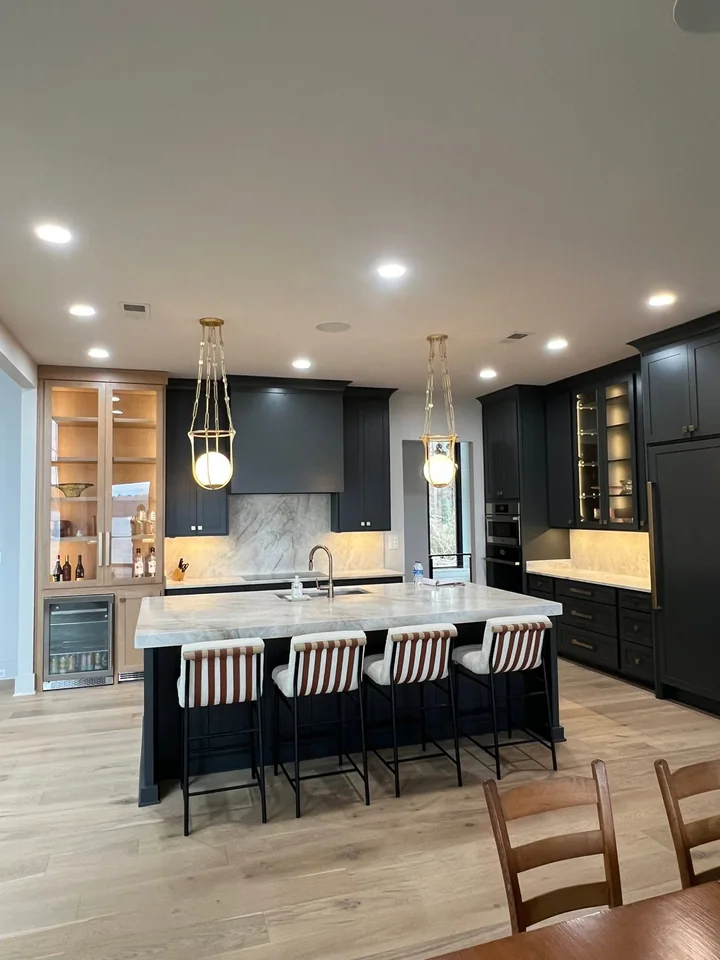 The Pickwick kitchen with charcoal cabinetry, warm display cabinets, a pale veined island and globe pendants.