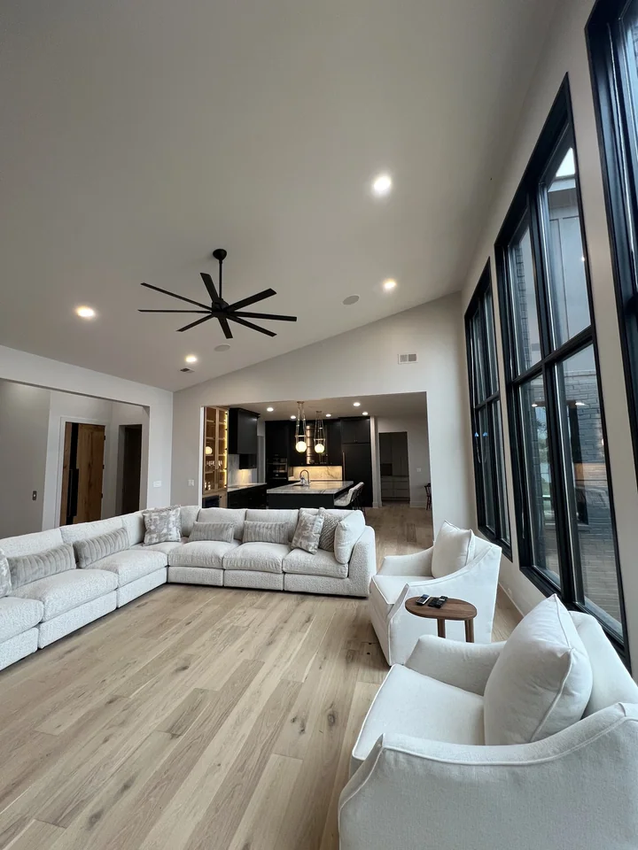 Pickwick’s living room with tall dark-framed windows, pale wood flooring, light seating and the kitchen visible beyond.