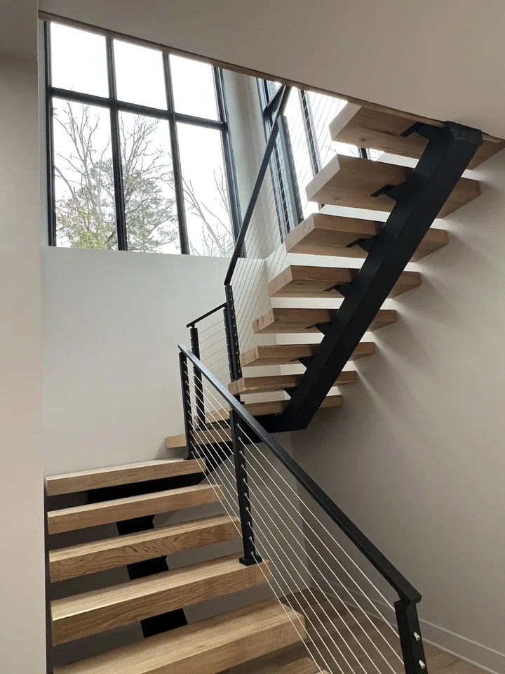The actual Pickwick staircase with wood treads, black steel supports and cable railing beside tall windows.
