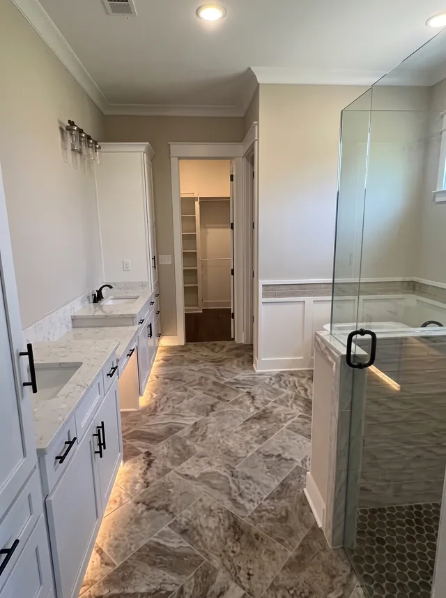 Pale vanity cabinetry, a glass shower and a boldly patterned stone floor.
