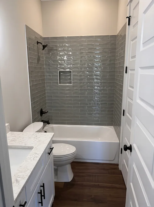 Gray tile wraps the bath beside a white vanity and paneled door.