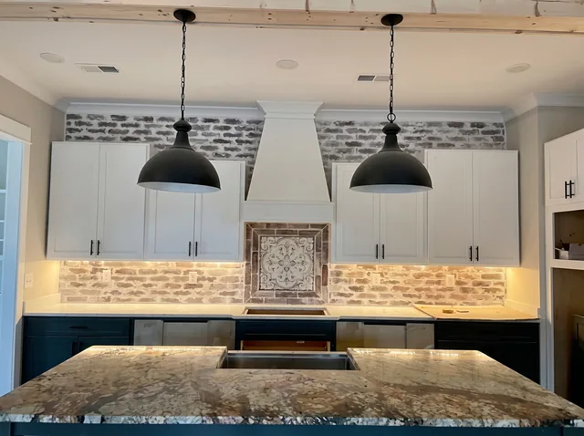 Blue-green cabinetry, a stone island and dark pendant lights.