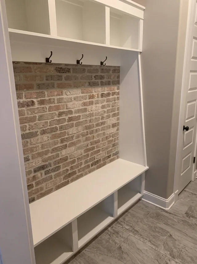 White storage and a bench sit against an exposed-brick backing.