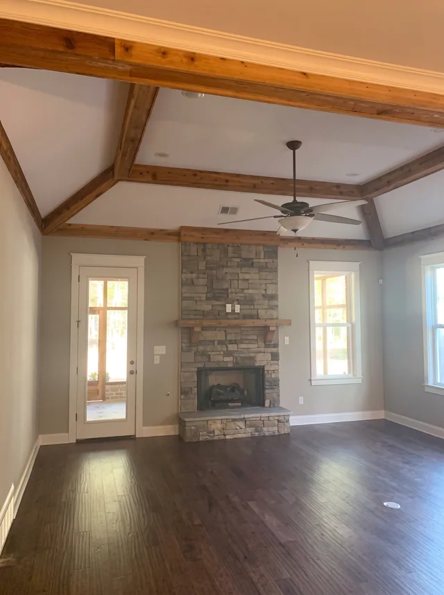 Timber ceiling beams frame a stone fireplace and adjoining windows.