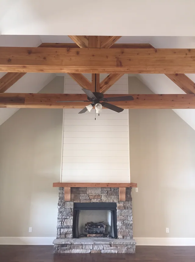 An exposed timber truss spans a stone hearth and white-planked chimney wall.