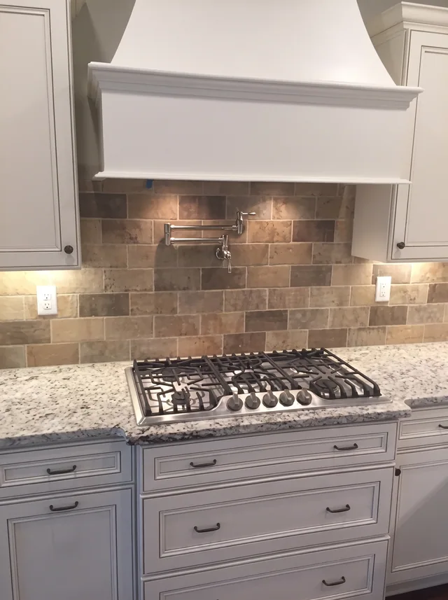 A pale range hood, cream cabinetry and stone backsplash surround the cooktop.
