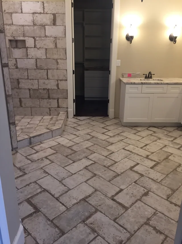 A stone-tiled shower and patterned floor sit beside a white vanity.