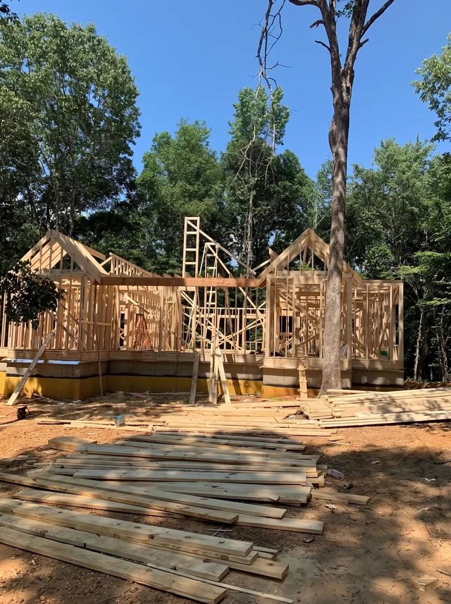 Timber wall and gable framing rises between mature trees.