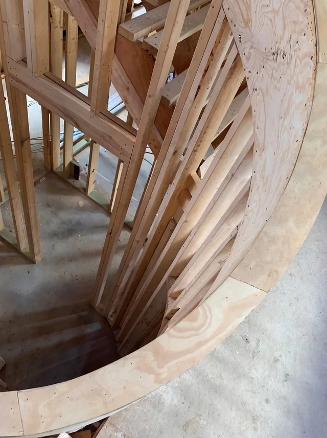 An overhead view reveals layers of plywood and timber around a curved stair.