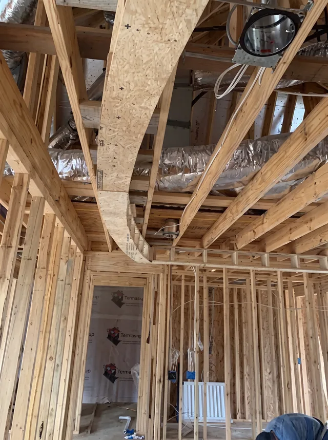 Curved timber and plywood framing meets exposed joists, ductwork and wiring.