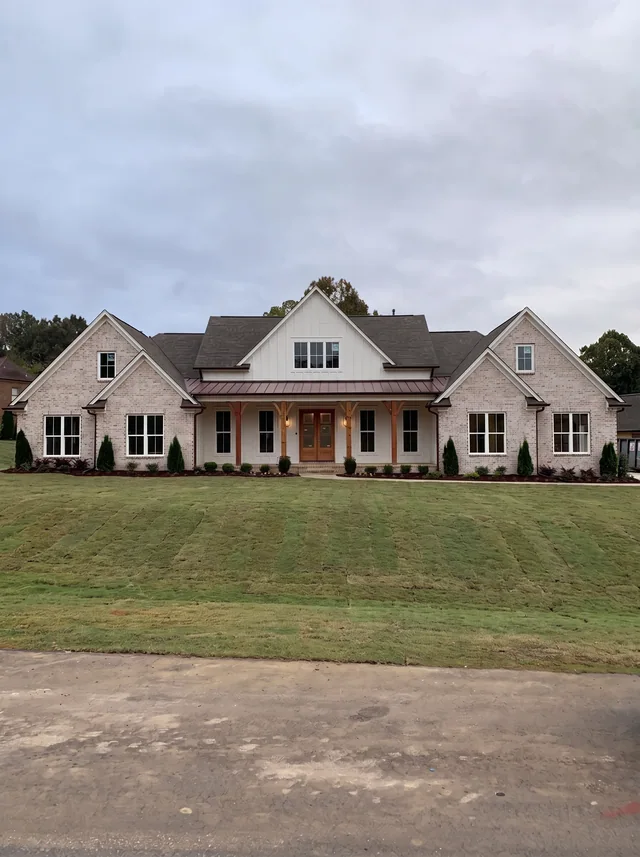 A broad gabled home and timber porch across a green lawn.