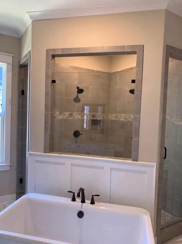 A freestanding bath sits before a glass-enclosed tiled shower and dark fittings.