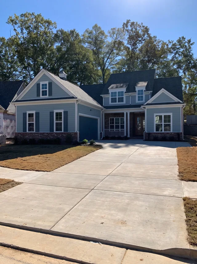 Blue-gray siding, brickwork and pale trim meet at the covered porch above a broad driveway.