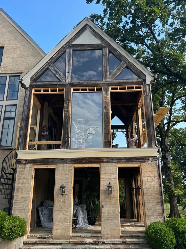Tall gable glazing rises above an open porch structure during construction.
