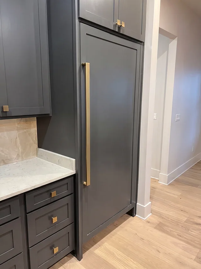 Dark cabinetry and a pale counter meet a tall cabinet beside an open doorway.