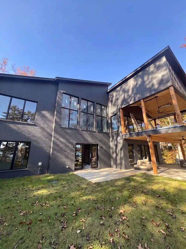 Tall windows and a timber-lined covered balcony face a sloping yard.