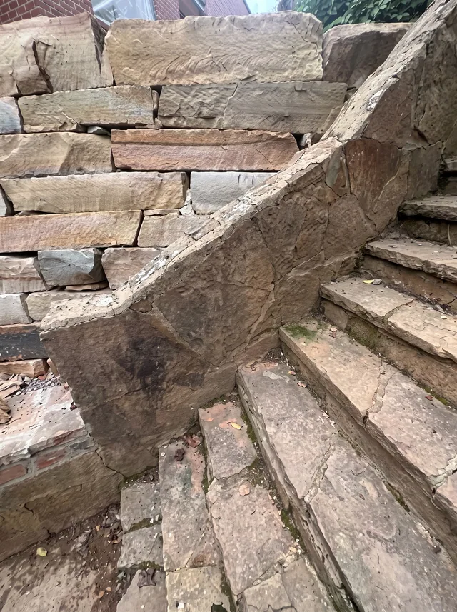 Stone steps run beside stacked retaining stones and a sloping garden edge.