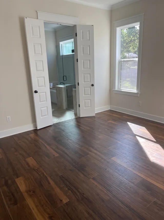 White-paneled doors open from a timber-floored room into an adjoining bathroom.