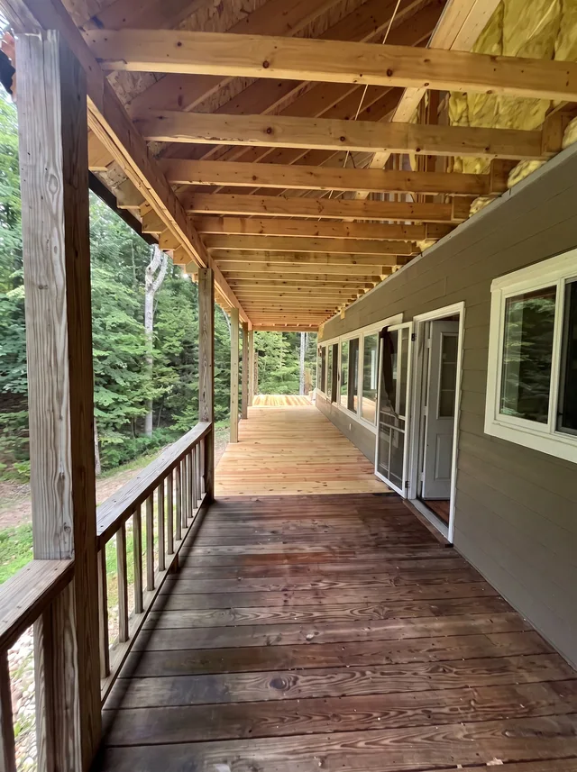 A timber-floored porch runs beneath exposed joists beside the house.